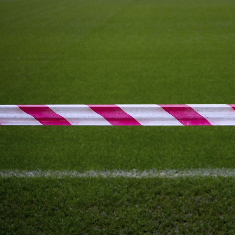 Red and white signal tape across a football pitch